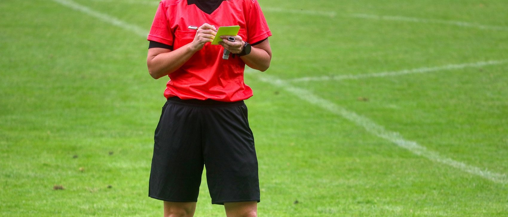Schiedsrichter im roten Trikot mit Notizblock auf dem Spielfeld